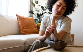 Young bored woman struggles to eat her breakfast while sitting on the her living room floor.